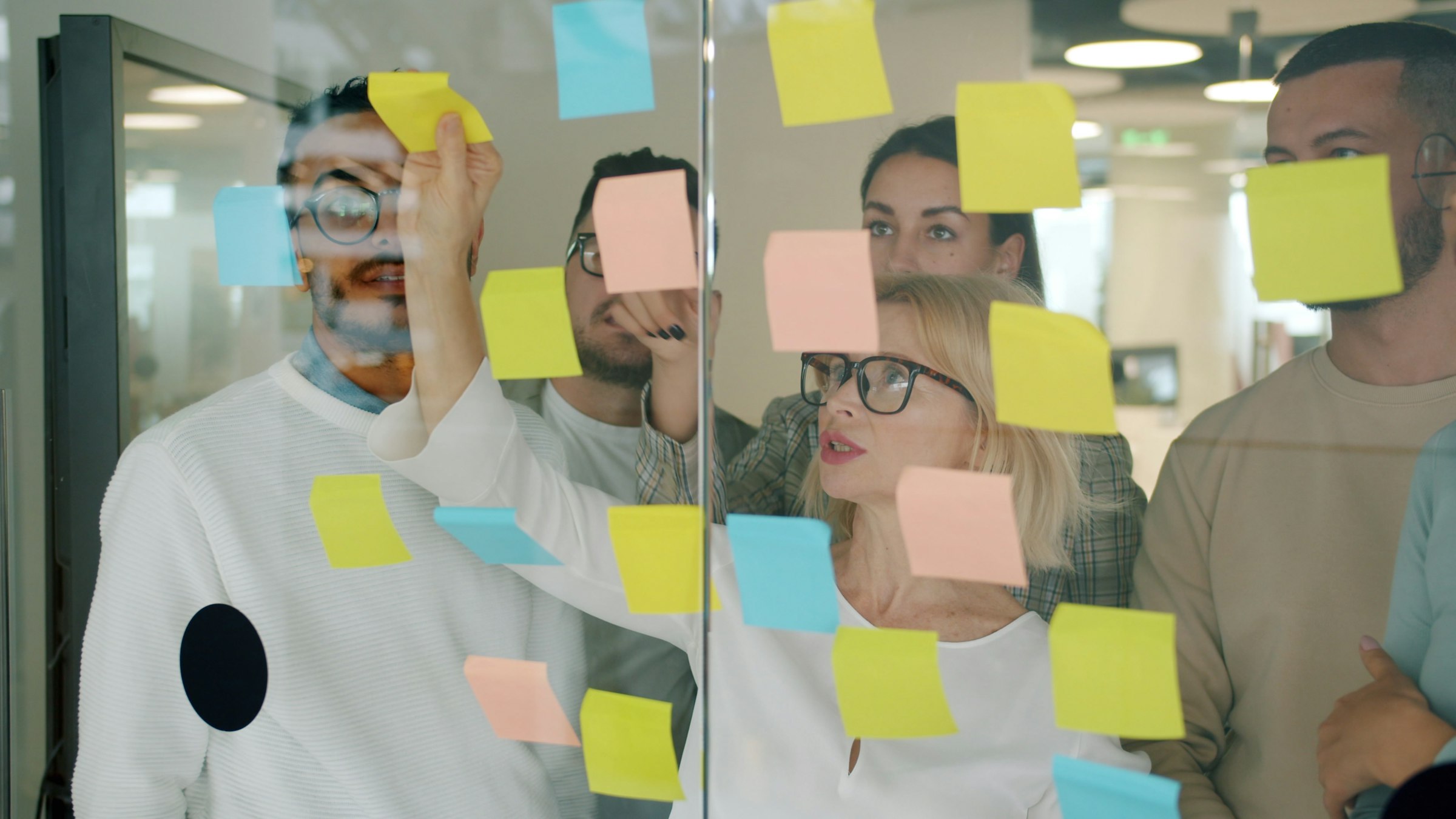 Team working through problems with sticky notes on a glass wall